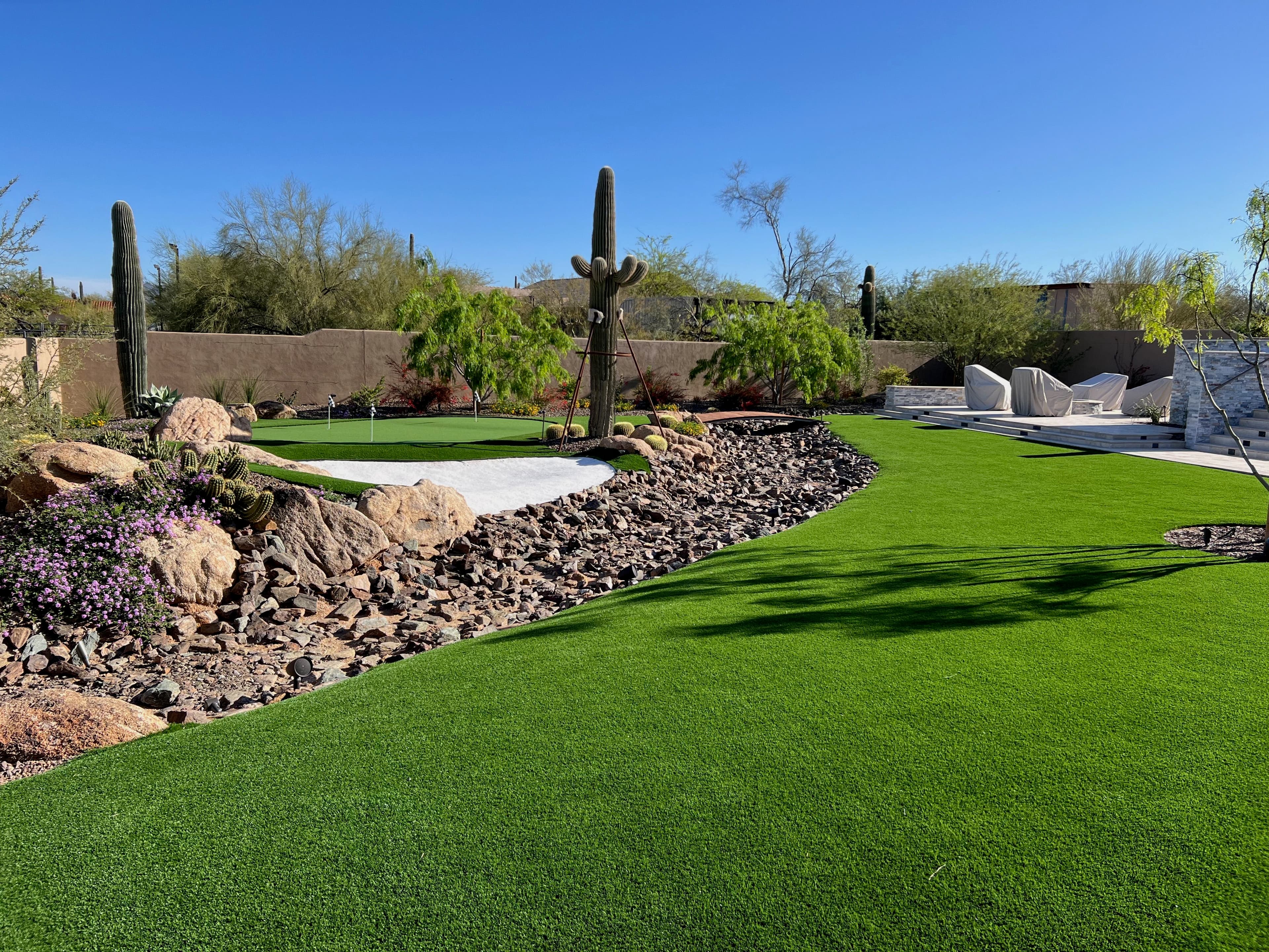 Desert landscape featuring artificial grass, cacti, and a modern outdoor seating area.