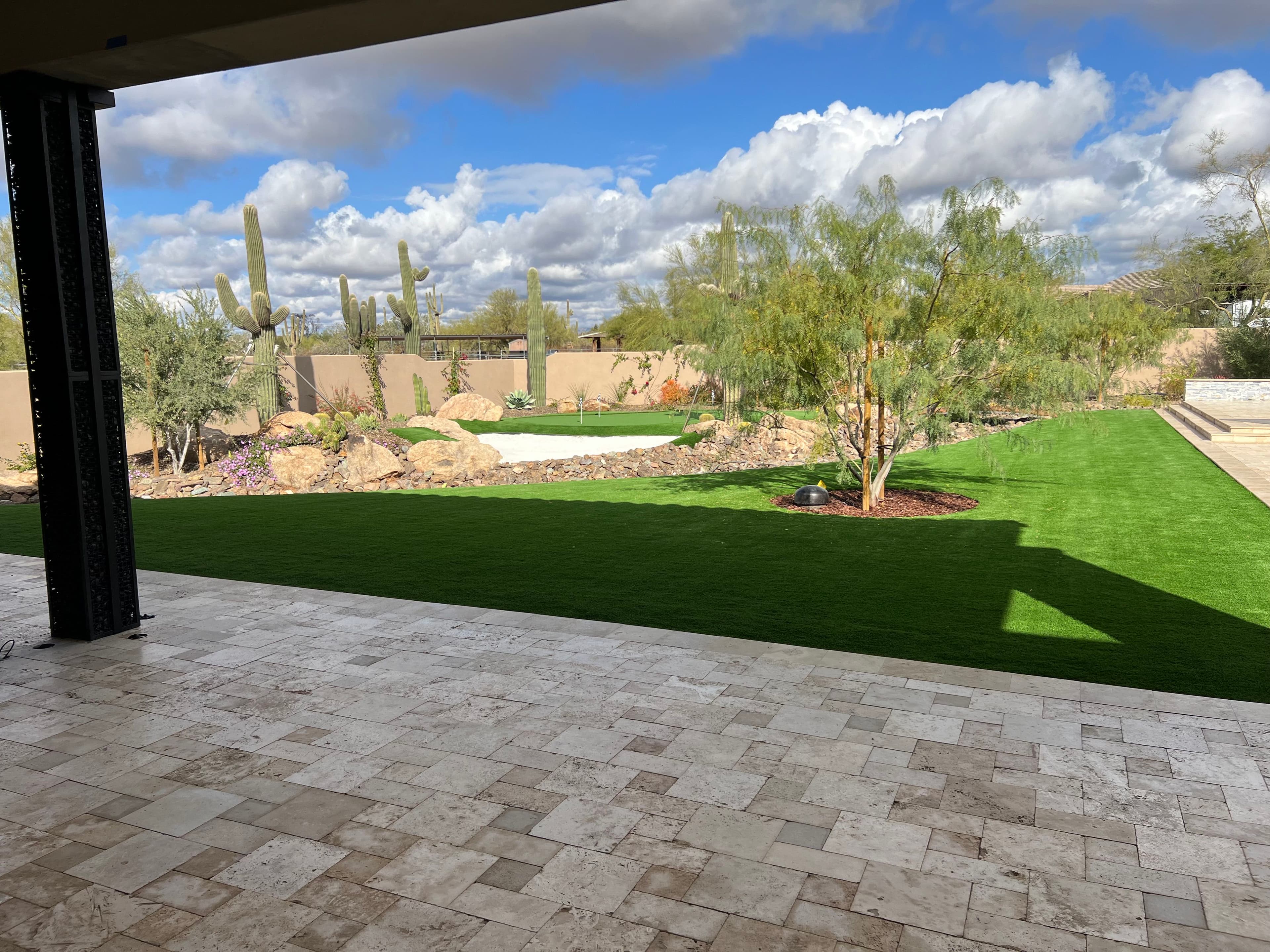 Lush green lawn and desert landscape featuring cacti under a bright sky with clouds.